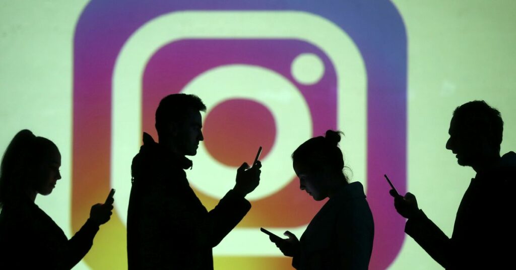 Silhouettes of mobile users are seen next to a screen projection of Instagram logo in this picture illustration taken March 28, 2018.  REUTERS/Dado Ruvic