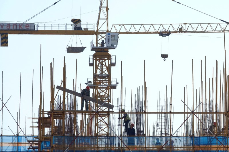 El signo de Vanke se ve encima de los trabajadores que trabajan en el sitio de construcción de un edificio residencial en Dalian, China.